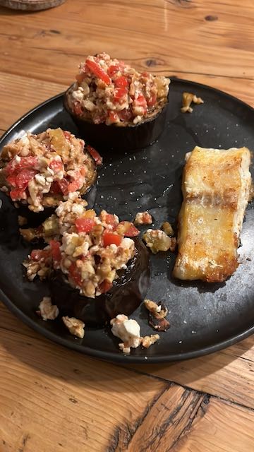 a black plate with three deliscious tomato topped eggplant towers and a fish steak