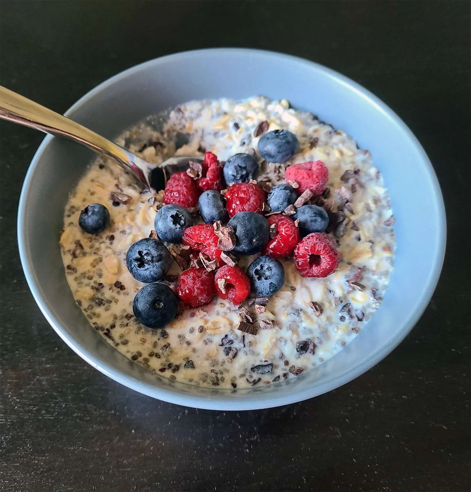 a bowl with overnight oats, berries, cacao nibs and spoon